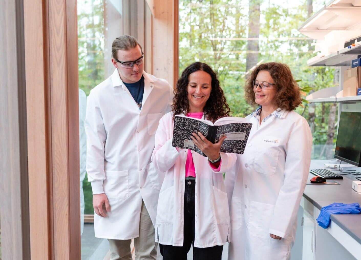 Three scientists in lab coats reviewing notes together in a modern laboratory space.
