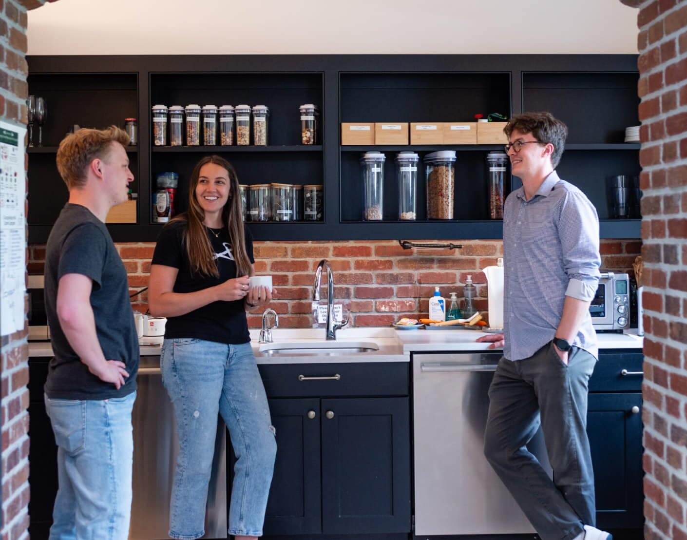 Three colleagues talking in a modern office kitchen.