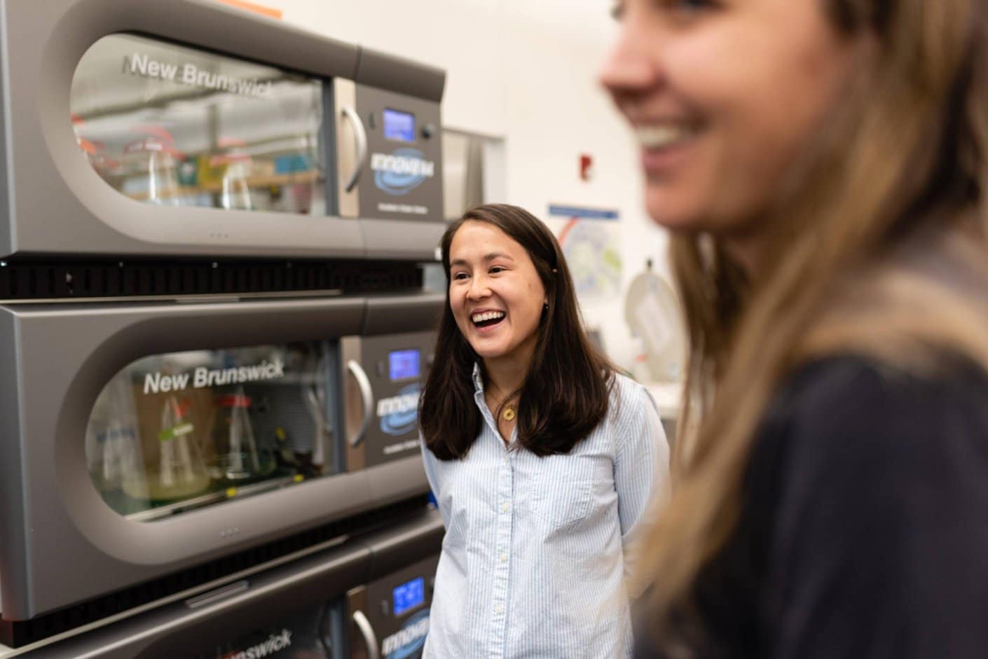 Scientist standing near laboratory shaking incubators with culture flasks inside.